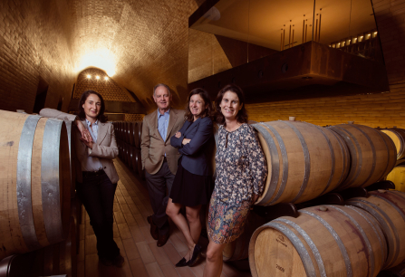 Vier Personen in einem eleganten Weinkeller mit hölzernen Weinfässern.