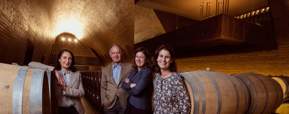 Vier Personen in einem eleganten Weinkeller mit hölzernen Weinfässern.