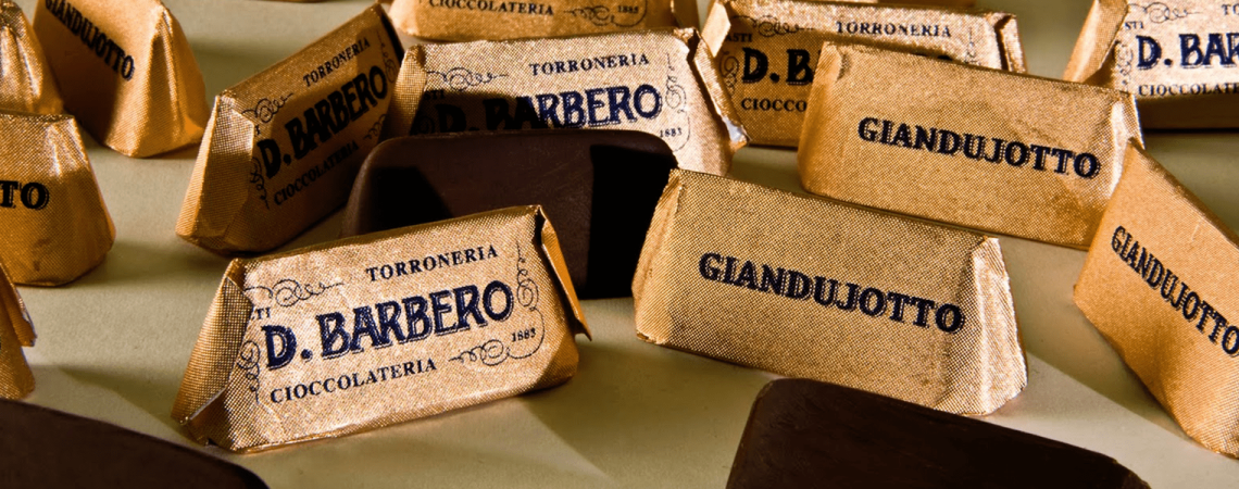 Goldene Pralinenverpackungen mit schwarzem Schriftzug auf hellem Hintergrund.