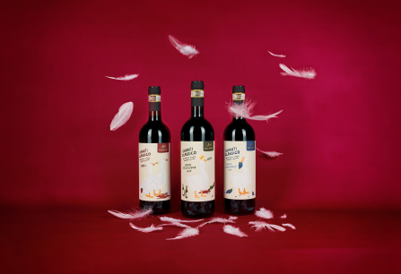 Drei Weinflaschen mit weißen Federn vor rotem Hintergrund.