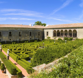 Historisches Herrenhaus mit großem Labyrinthgarten und gepflegtem Weinberg unter blauem Himmel.