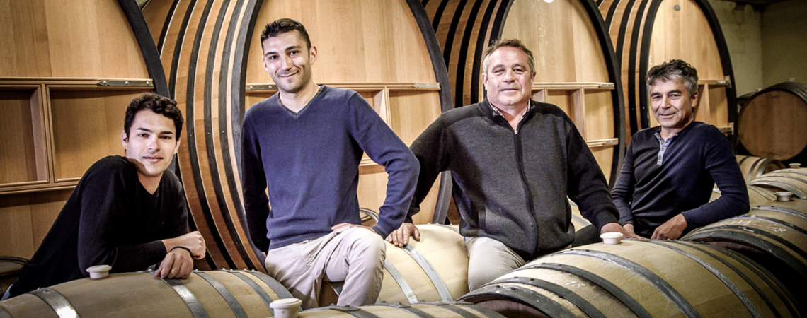 Vier Männer lehnen an großen Weinfässern in einem Weinkeller.