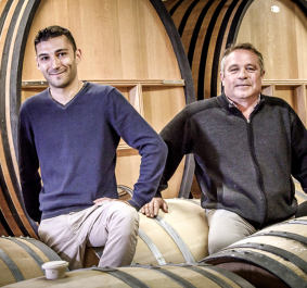 Vier Männer lehnen an großen Weinfässern in einem Weinkeller.