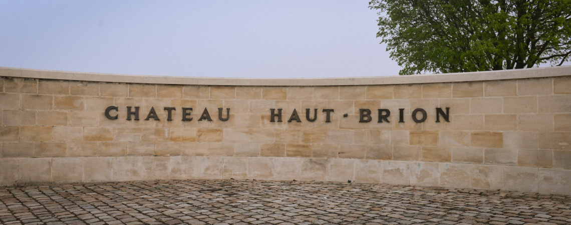 Natursteinmauer mit Schriftzug, Pflastersteine im Vordergrund, Baum rechts im Hintergrund.