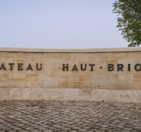 Natursteinmauer mit Schriftzug, Pflastersteine im Vordergrund, Baum rechts im Hintergrund.