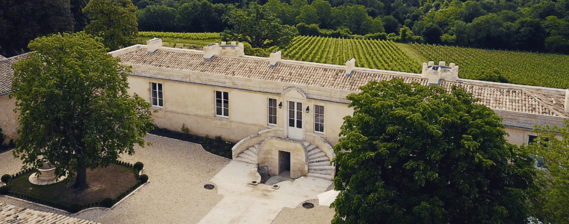 Historisches Steingebäude mit luxuriösen Treppen, umgeben von üppigen Weinbergen und Bäumen.