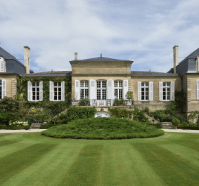 Historisches Herrenhaus mit großen Fenstern, flankiert von gepflegtem Rasen und üppigem Garten.