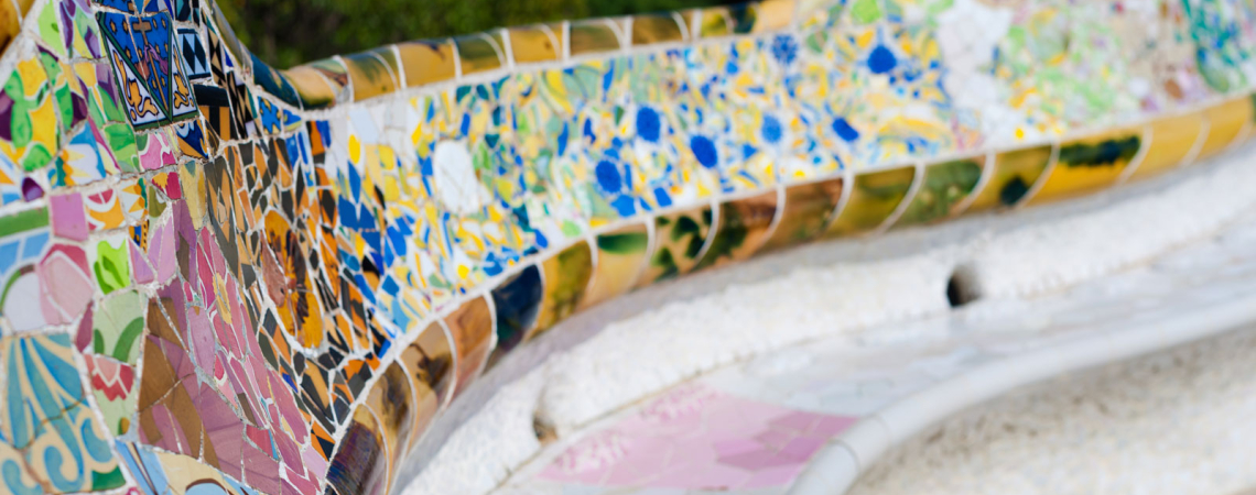 Bunte, geschwungene Mosaikbank mit floralen und geometrischen Mustern im Freien.