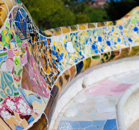 Bunte, geschwungene Mosaikbank mit floralen und geometrischen Mustern im Freien.