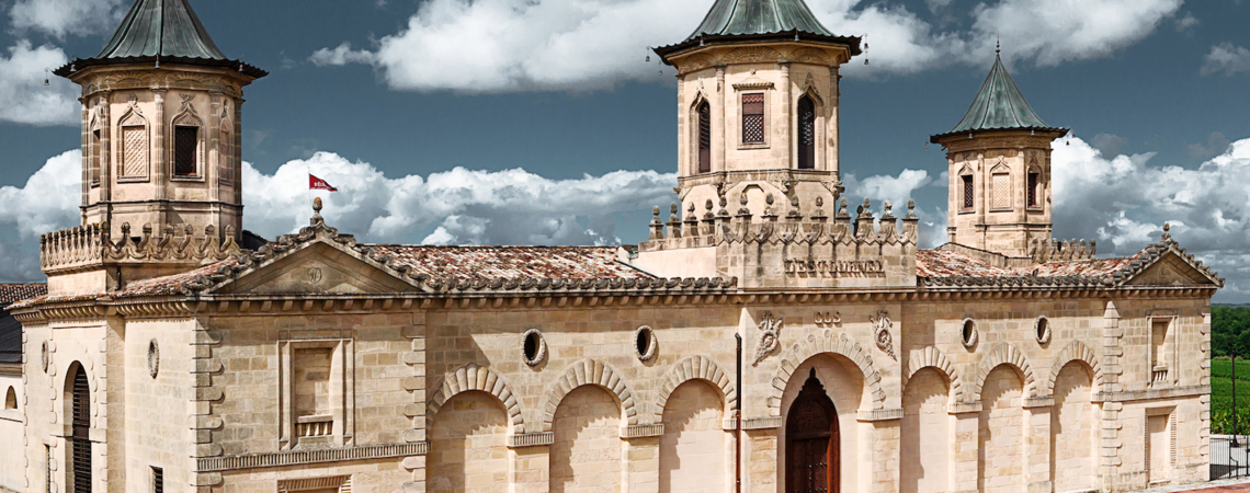 Historisches Gebäude mit symmetrischen Türmen, gelben Steinmauern und rotem Ziegeldach.