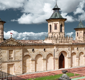 Historisches Gebäude mit symmetrischen Türmen, gelben Steinmauern und rotem Ziegeldach.
