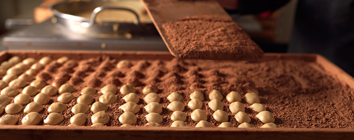 Person schichtet weiße Schokokugeln in Kakaopulver auf Tablett.
