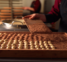 Person schichtet weiße Schokokugeln in Kakaopulver auf Tablett.