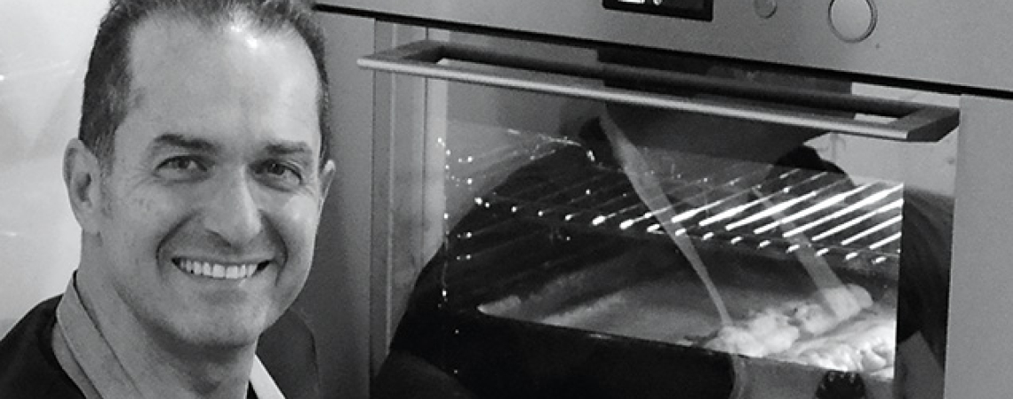 Mann lächelt vor einem modernen Backofen mit Sichtfenster.