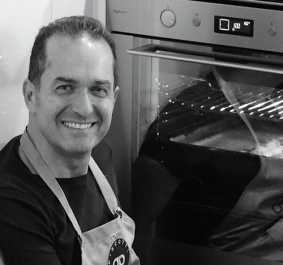Mann lächelt vor einem modernen Backofen mit Sichtfenster.