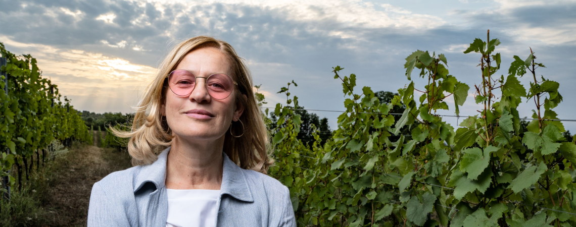 Frau mit rosafarbener Brille steht in einem sonnenbeschienenen Weinberg.