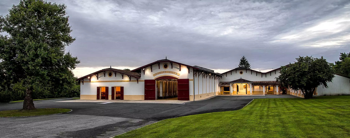 Großes, rustikales Gebäude mit symmetrischer Fassade und gepflegtem Rasen unter dramatischem Himmel.