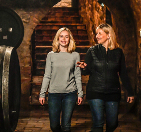 Zwei Personen gehen lächelnd durch einen historischen Weinkeller mit brennenden Kerzen.