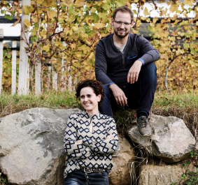 Zwei Personen sitzen auf Steinen vor herbstlichen Weinreben.