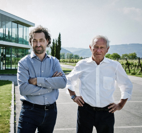 Zwei Männer vor einem modernen Gebäude in einer Weinberglandschaft.