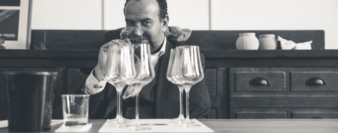 Mann bei Weinverkostung mit mehreren Gläsern in gemütlicher, rustikaler Umgebung.