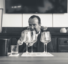 Mann bei Weinverkostung mit mehreren Gläsern in gemütlicher, rustikaler Umgebung.