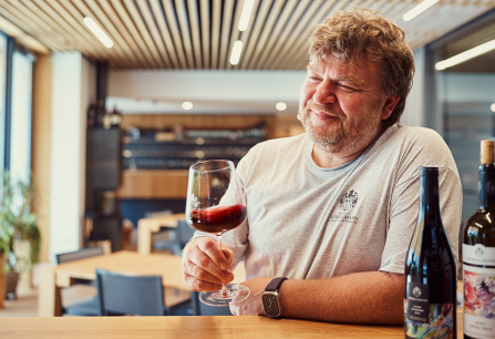 Mann verkostet Wein in modernem, holzverkleidetem Raum mit Flaschen auf dem Tisch.