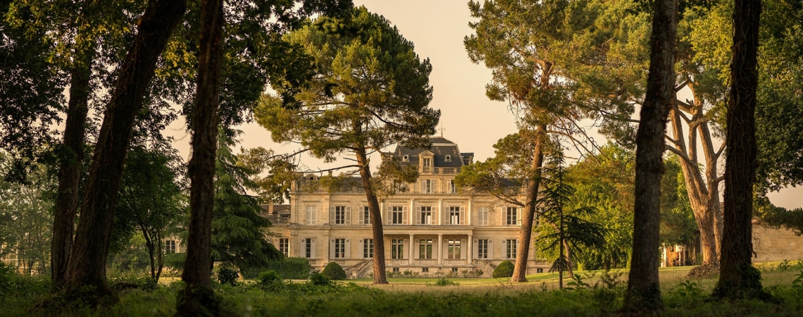 Historisches Herrenhaus hinter Bäumen, von warmem Licht umgeben.