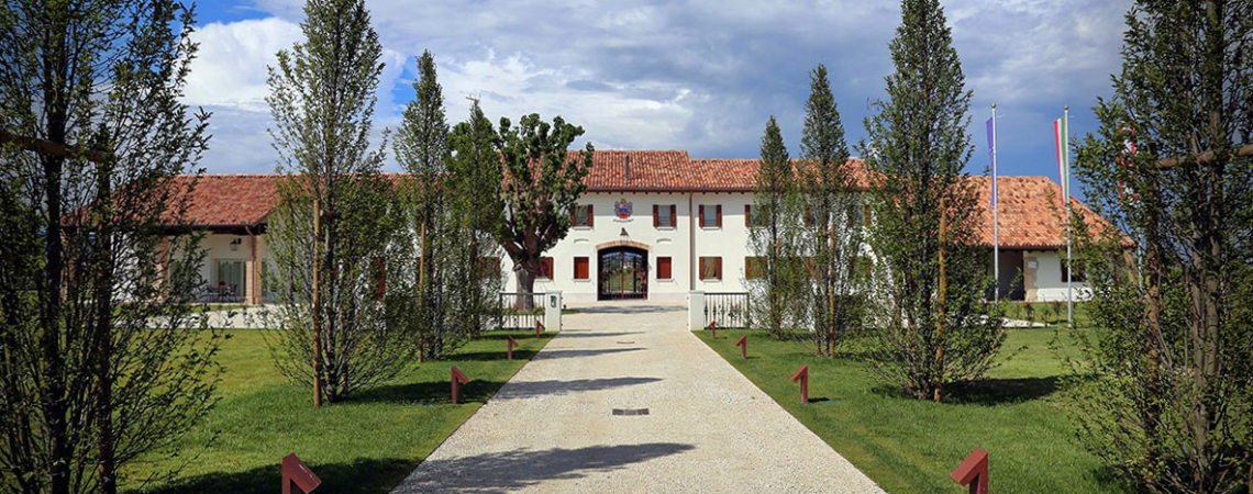 Großes Gebäude mit rotem Dach, Kiesweg und Bäumen, unter blauem Himmel.