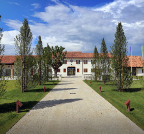 Großes Gebäude mit rotem Dach, Kiesweg und Bäumen, unter blauem Himmel.