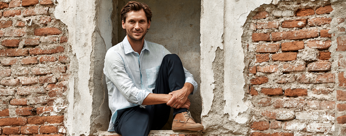 Mann in hellem Hemd sitzt lässig in verfallener Backsteinmauer.