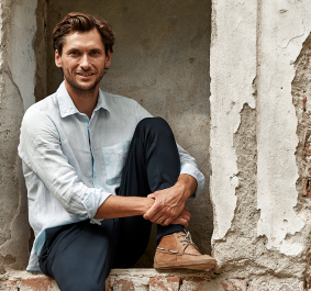 Mann in hellem Hemd sitzt lässig in verfallener Backsteinmauer.