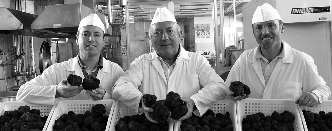 Drei Männer in weißen Kitteln halten Körbe voller Trüffel.