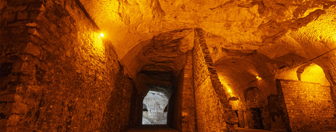 Beleuchteter, steinerner Tunnel mit gewölbter Decke und warmem Licht.