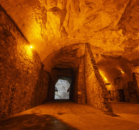 Beleuchteter, steinerner Tunnel mit gewölbter Decke und warmem Licht.