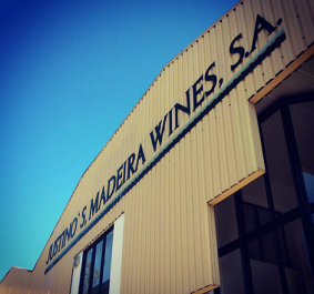 Beiges Industriegebäude mit Glasfenstern und blauem Himmel im Hintergrund.