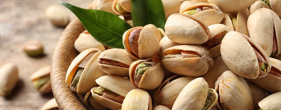 Nahaufnahme von Pistazien in einer hölzernen Schale mit grünen Blättern.