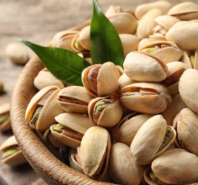 Nahaufnahme von Pistazien in einer hölzernen Schale mit grünen Blättern.