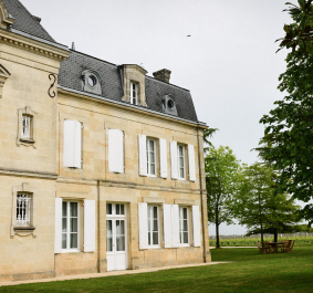 Historisches Herrenhaus mit grauem Dach in grüner Gartenlandschaft.