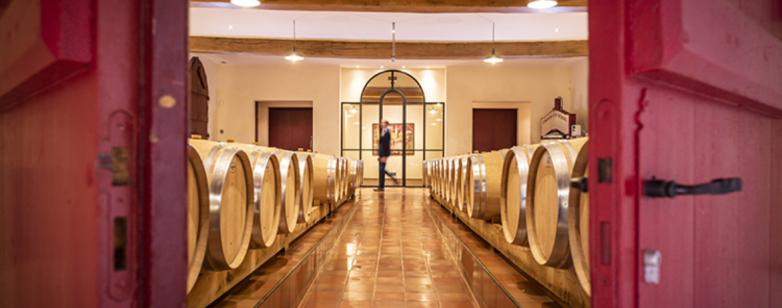 Roter Türrahmen öffnet Blick in Weinkeller mit Holzfässern und gefliesten Boden.