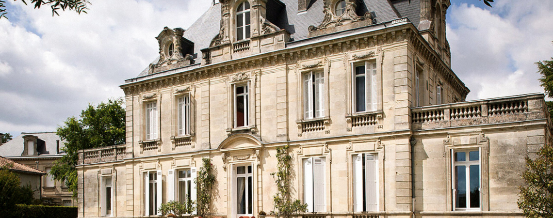 Historisches Herrenhaus mit klassischer Fassade und großen Fenstern, umgeben von Garten.