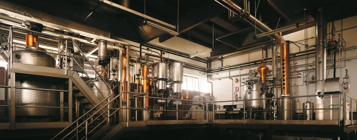 Industrielle Destillationsanlage mit glänzenden Kupfer- und Edelstahltanks in beleuchtetem Raum.