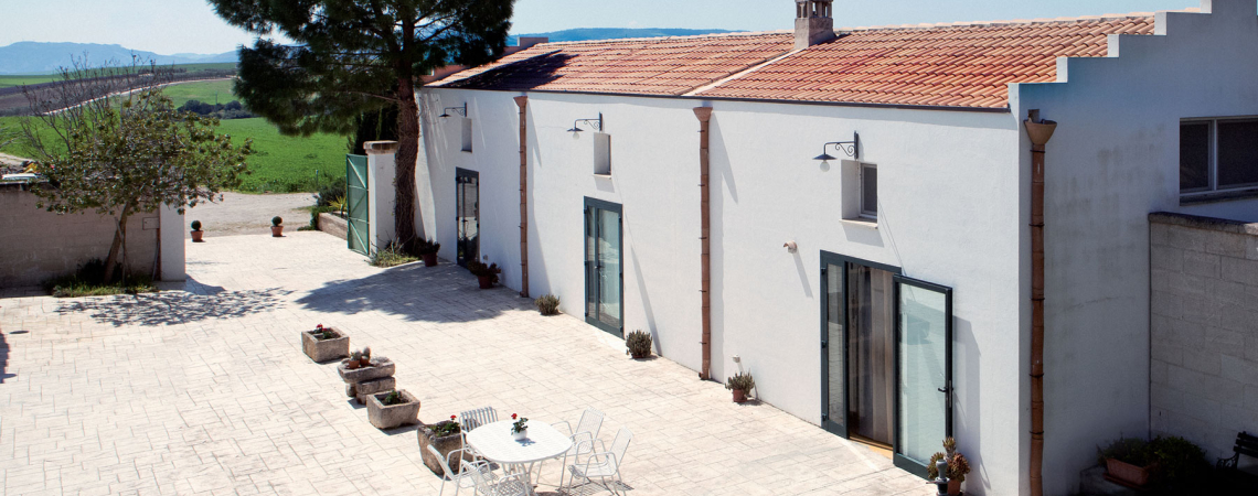 Weißes Gebäude mit Ziegeldach und Innenhof, umgeben von grüner Landschaft.