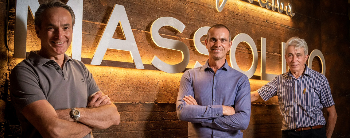 Drei Männer vor beleuchtetem Schriftzug auf einer Backsteinwand.