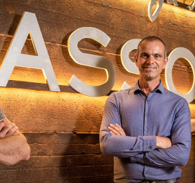 Drei Männer vor beleuchtetem Schriftzug auf einer Backsteinwand.