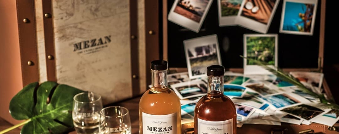 Zwei Rumflaschen vor Vintage-Koffer mit Reisefotos und tropischen Dekorationen.