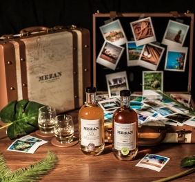 Zwei Rumflaschen vor Vintage-Koffer mit Reisefotos und tropischen Dekorationen.