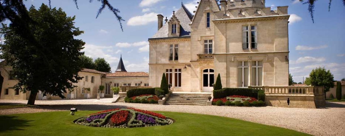Historisches Schloss mit gepflegtem Garten und Blumenbeet bei strahlendem Wetter.