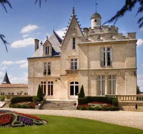 Historisches Schloss mit gepflegtem Garten und Blumenbeet bei strahlendem Wetter.