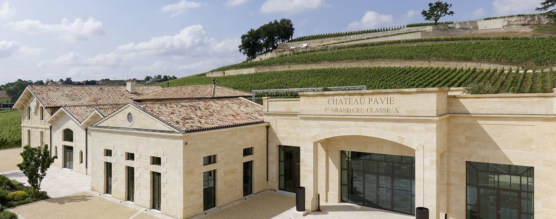 Helles Gebäude mit Bögen, umgeben von Weinbergen und blauem Himmel.